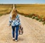 woman walking down dirt road with suit case.